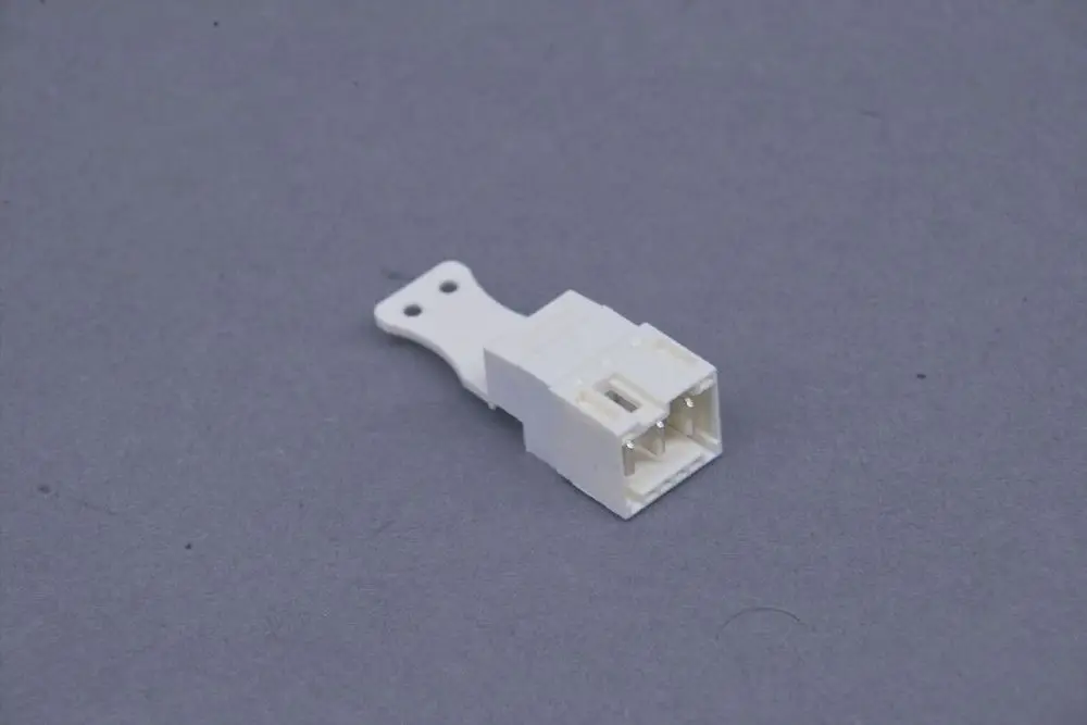 Weißer Stecker mit zwei Anschlüssen und einer Halterung, hergestellt von Brötje, auf grauem Hintergrund.