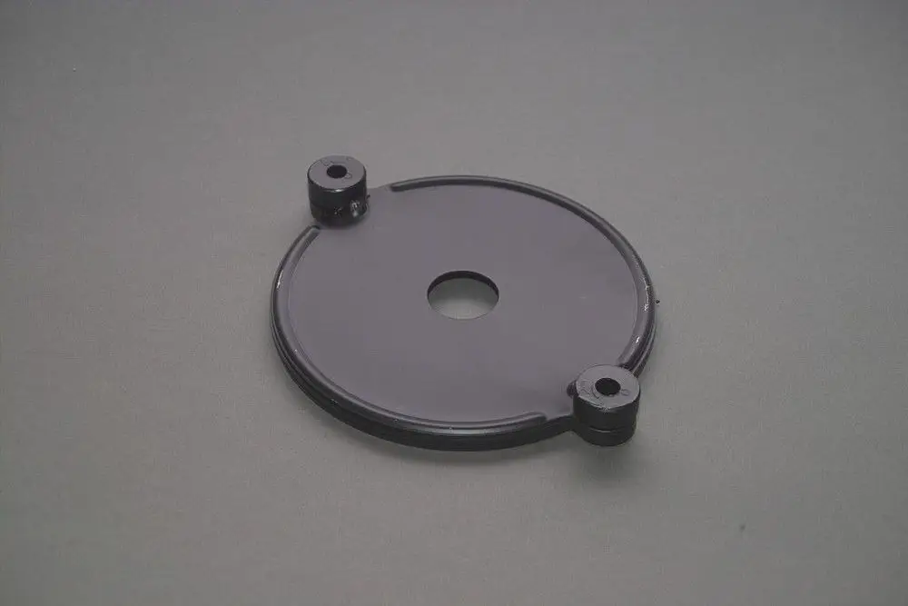 Schwarze runde Metallplatte mit mittigem Loch und zwei seitlichen Halterungen. Teil eines Brötje-Produkts für einen Motor oder Ventilator.