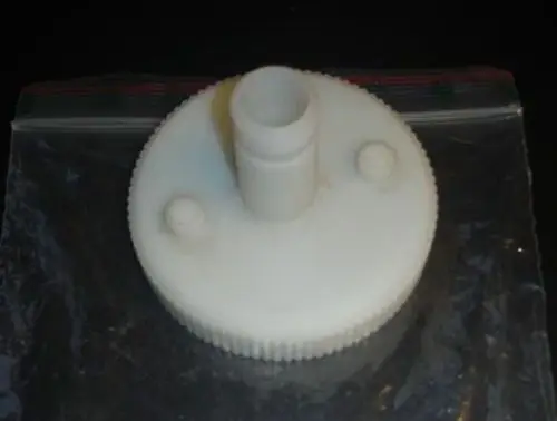 Weißer Kunststoffdeckel mit Messöffnung und einem zentralen Stecker. Der Deckel hat eine gezähnte Kante und ist mit zwei kleinen Erhöhungen versehen. Produkt von Brötje.