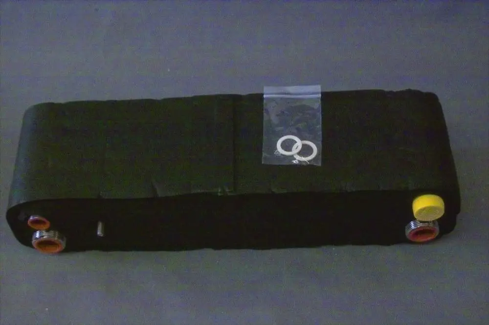 Brötje Wärmetauscher in schwarzer und kompakter Bauform mit verschiedenen Anschlussöffnungen und einer Tüte mit zwei Dichtungsringen oben auf.