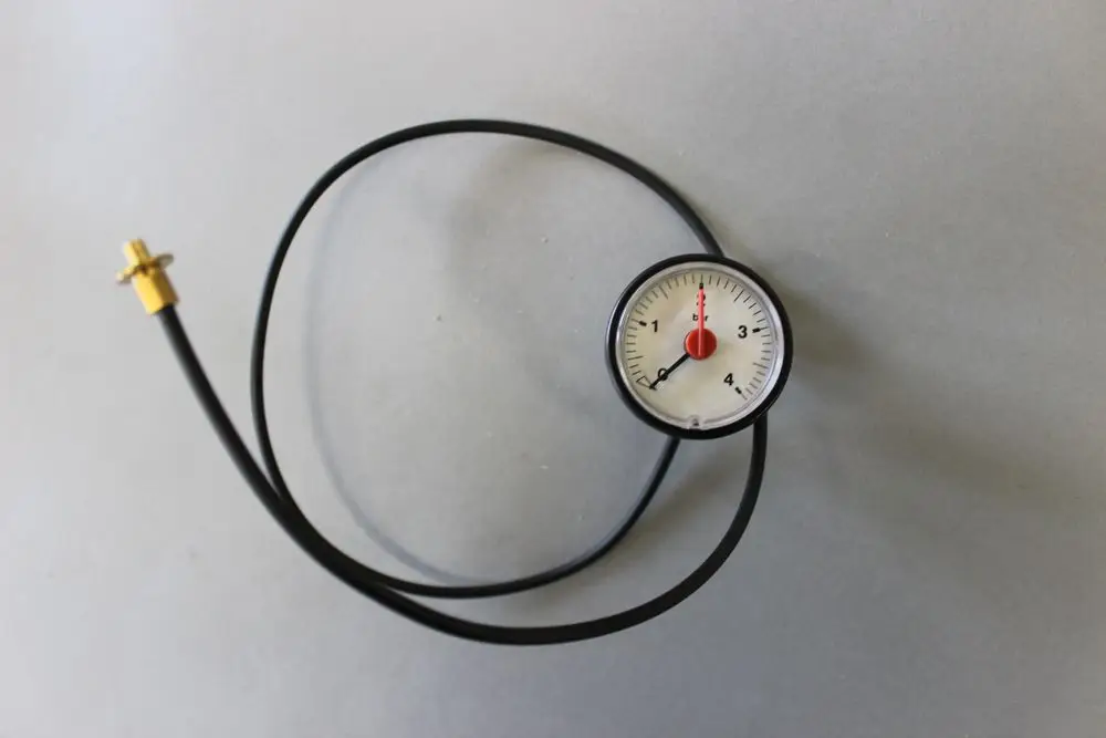 Manometer mit einem Ziffernblatt und einem schwarzen Schlauch, verbunden mit einem goldenen Anschluss. Produkt von Brötje zur Druckmessung.