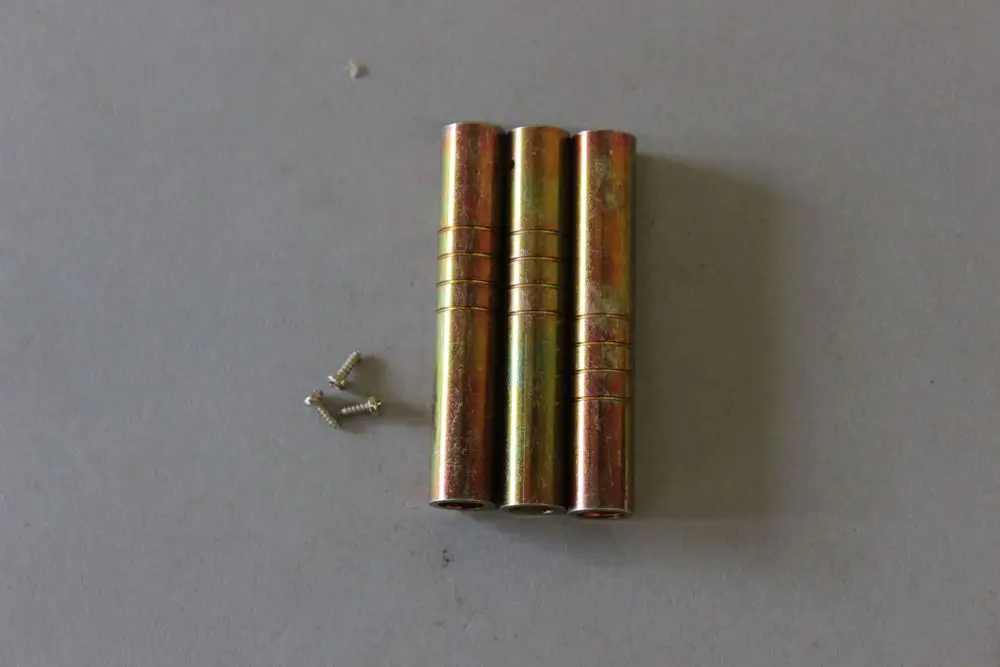 Drei metallene Zylinder in goldfarbener Oberfläche, daneben zwei kleine Schrauben. Möglicherweise Teile eines Gaskopfes von Brötje.