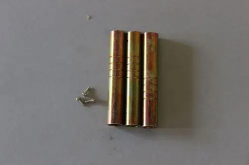 Drei metallene Zylinder in goldfarbener Oberfläche, daneben zwei kleine Schrauben. Möglicherweise Teile eines Gaskopfes von Brötje.