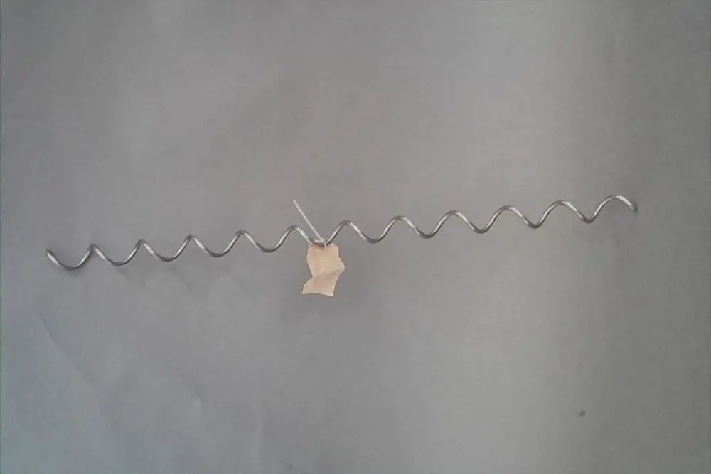 Brötje Wirbulator aus Metall mit wellenförmiger Struktur, mit einem Anhänger aus Papier zur Kennzeichnung, auf grauem Hintergrund.