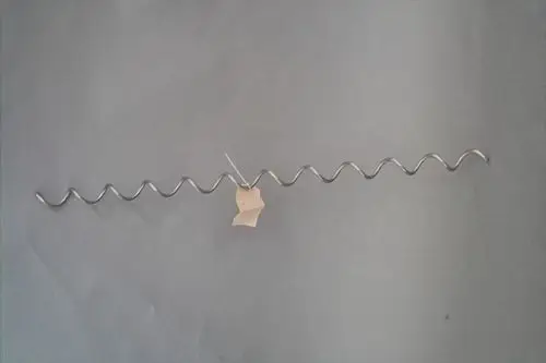 Brötje Wirbulator aus Metall mit wellenförmiger Struktur, mit einem Anhänger aus Papier zur Kennzeichnung, auf grauem Hintergrund.