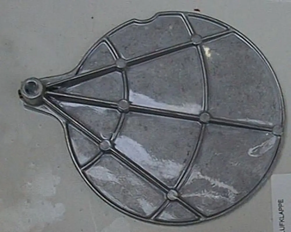 Metallische Luftklappe von Brötje, kreisförmig mit mehreren Rippenelementen und einem Befestigungsansatz, auf hellem Hintergrund.