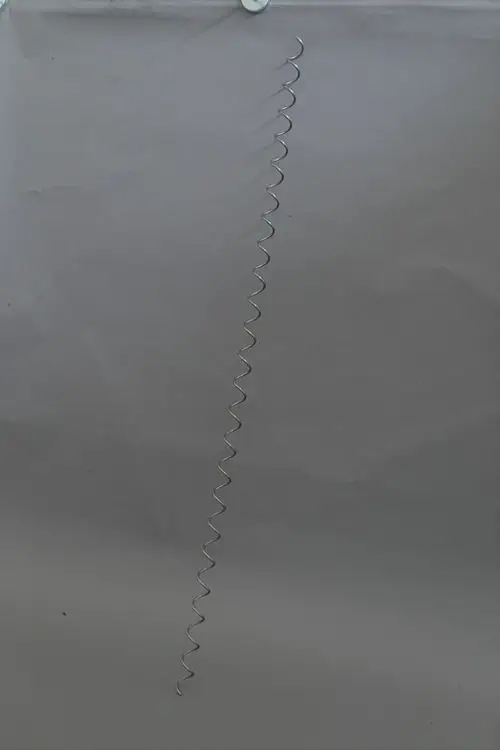Schraubenförmiger Wirbulator aus Metall, montiert an einer Aufhängung, vor grauem Hintergrund. Produkt von Brötje.