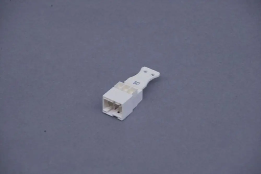 Weißer Kunststoffstecker von Brötje mit mehreren Kontaktstiften und einem Halteclip, auf grauem Hintergrund.