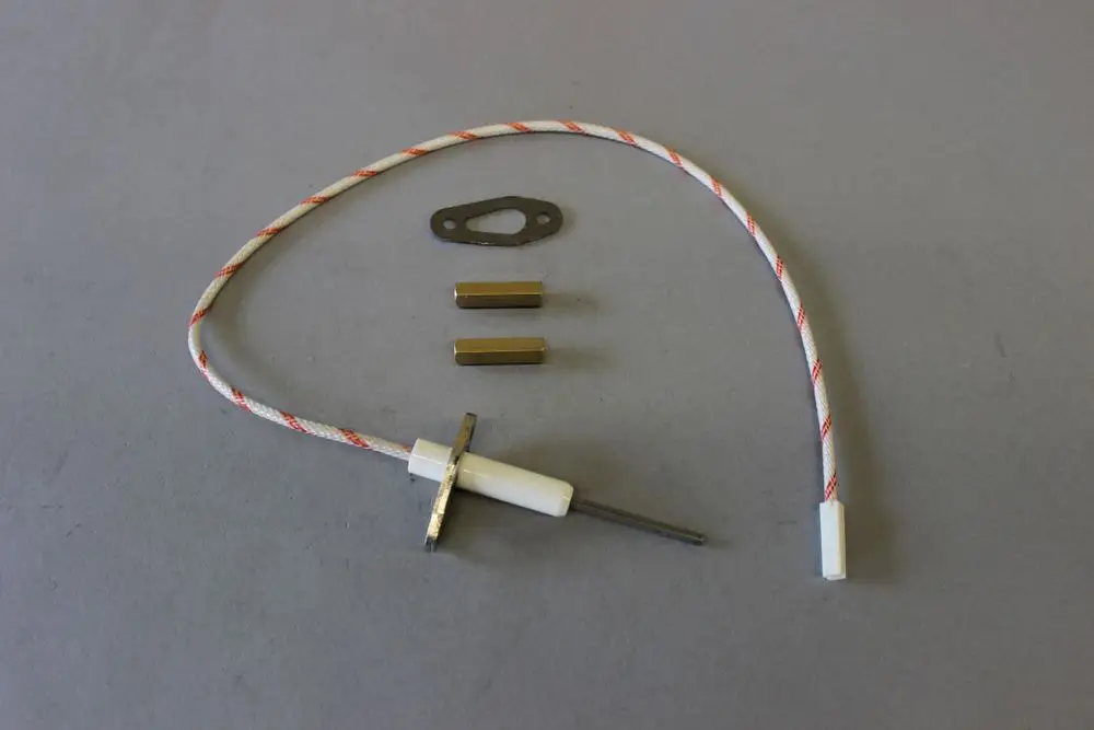 Brötje Ionisationselektrode mit Verbindungselementen und Kabel. Komponenten in neutralen Farben auf grauem Untergrund angeordnet.