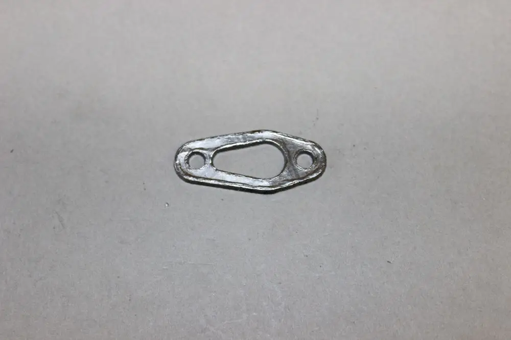 Metallische Dichtung mit durchgehend ovalem Loch und zwei Befestigungslöchern, möglicherweise für die Zündelektrode von Brötje-Geräten.