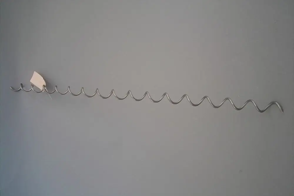 Brötje Wirbulator aus Metall, gewunden in gleichmäßigen Wellen, montiert an einer grauen Wand. Ein preisschild hängt an einem der Wellen.