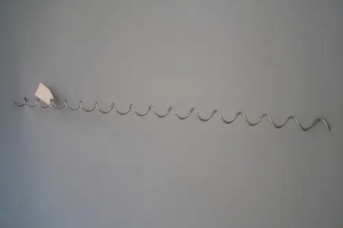 Brötje Wirbulator aus Metall, gewunden in gleichmäßigen Wellen, montiert an einer grauen Wand. Ein preisschild hängt an einem der Wellen.