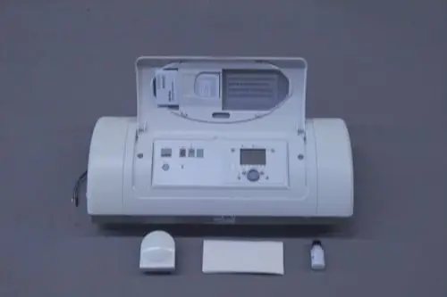 Brötje Regelung mit digitalem Display und mehreren Tasten, dazu Sensor und kleines Fläschchen, auf einem grauen Untergrund angeordnet.