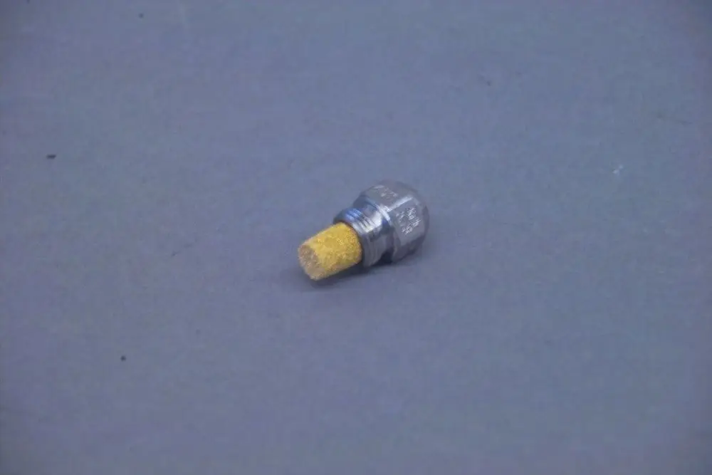 Brötje-Düse aus Metall mit einem gelben, porösen Ende, liegt auf grauem Hintergrund. Die Verbindung ist gewindeartig und zeigt keine spezifischen Maße oder Typen.