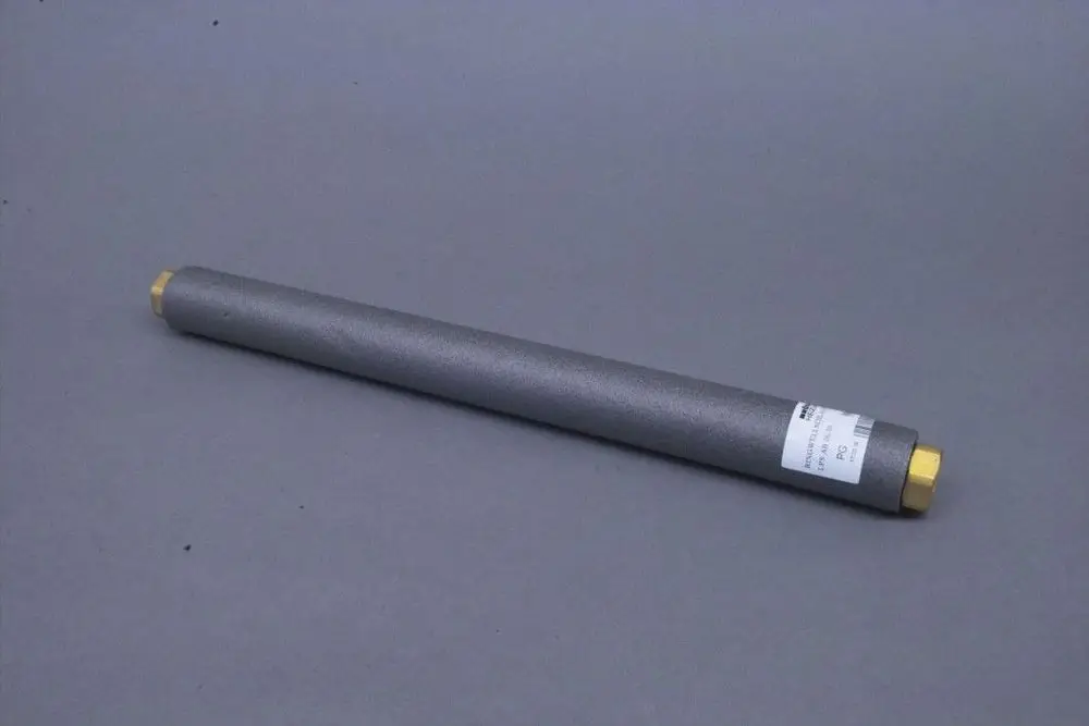 Grauer, zylindrischer Schlauch mit zwei abgerundeten Enden, einer in Messing, Beschriftung auf einem Etikett, liegend auf grauem Untergrund. Produkt von Brötje.
