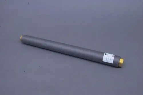 Grauer, zylindrischer Schlauch mit zwei abgerundeten Enden, einer in Messing, Beschriftung auf einem Etikett, liegend auf grauem Untergrund. Produkt von Brötje.