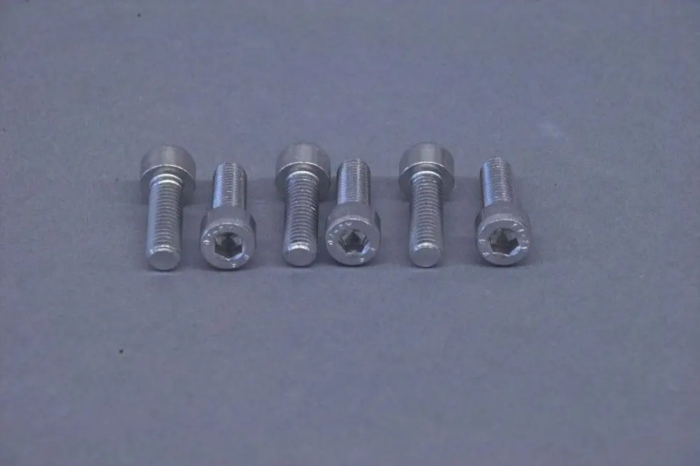 Brötje Schrauben-Set mit mehreren Metall-Schrauben, die eine Sekundäraufnahme für Inbus-Schraubenzüge aufweisen, angeordnet in einer Reihe auf grauem Hintergrund.