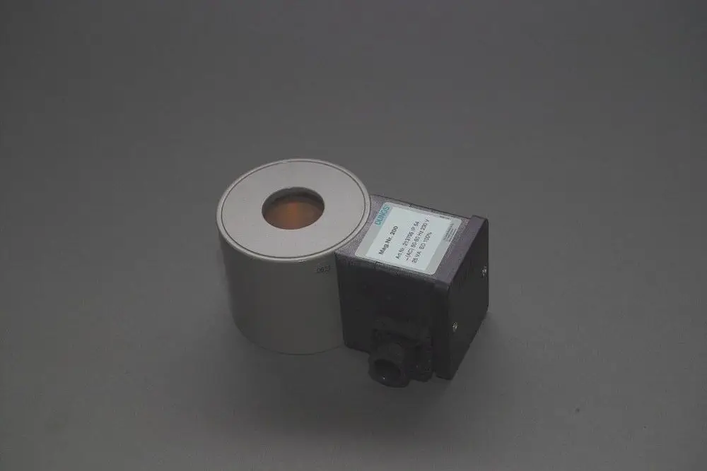 Brötje Magnetspule, rechteckiges schwarzes Gehäuse mit einem runden silbernen Element, ausgestattet mit einer transparenten Öffnung, auf grauem Untergrund.