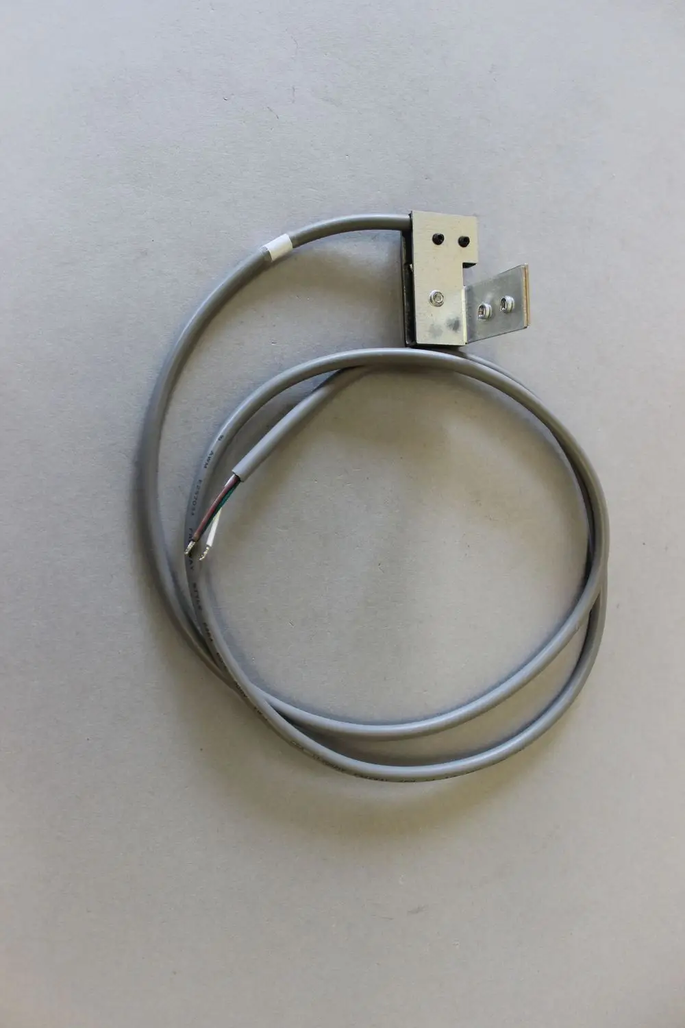 Brötje Schalter mit grauem Kabel und Metallhalterung auf grauem Untergrund. Zwei Kabelenden sind sichtbar, eines mit freiliegenden Drahtenden.