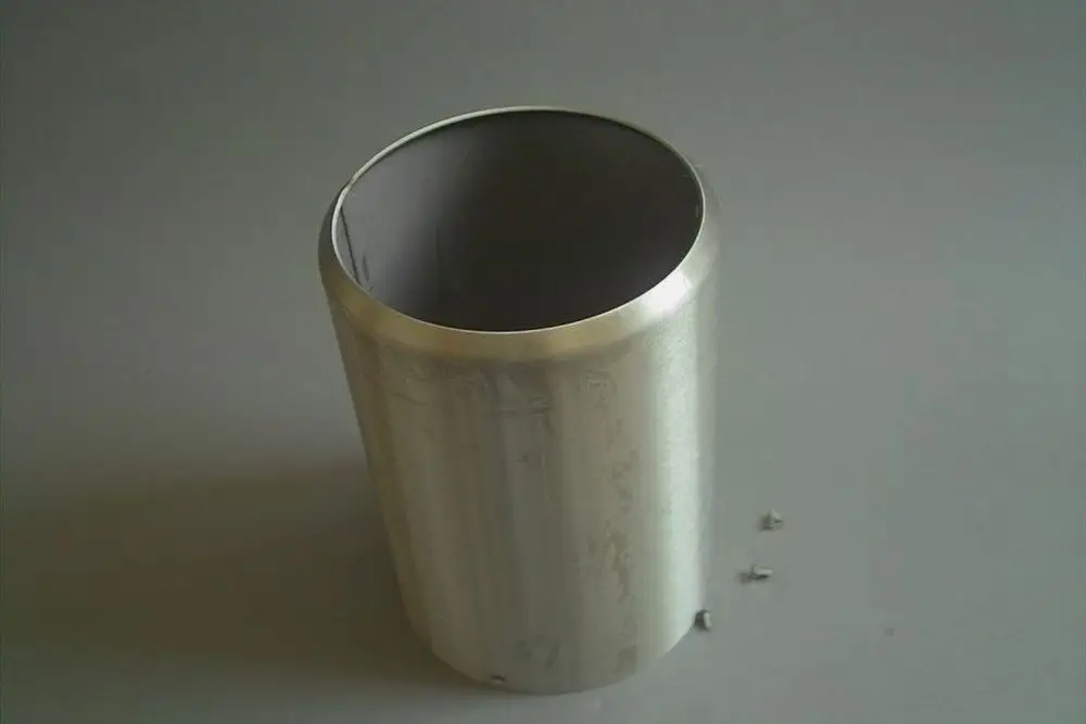 Edelstahlröhre mit glatter Oberfläche, geöffnet an der Oberseite. Neben der Röhre liegen einige kleine Schrauben. Produkt von Brötje, möglicherweise für Heizungssysteme.