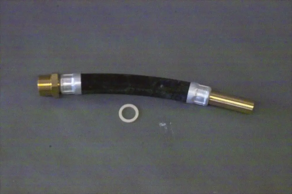 Brötje Rücklaufrohr aus schwarzem Schlauch mit goldfarbenen und weißen Verbindungsteilen, begleitet von einem weißen O-Ring auf grauem Hintergrund.