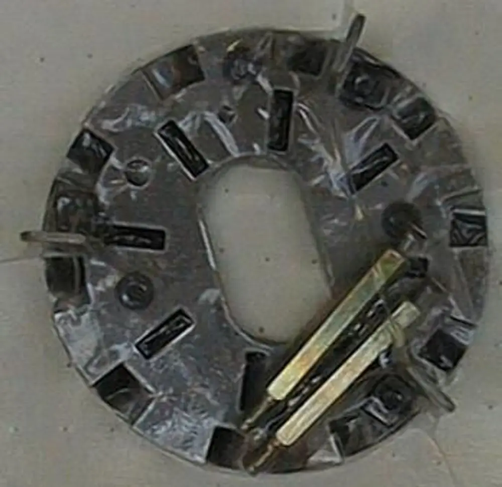 Metallische Stauscheibe von Brötje, oval, mit mehreren Aussparungen und Holzklötzen an der Seite, auf einem hellen Untergrund abgebildet.