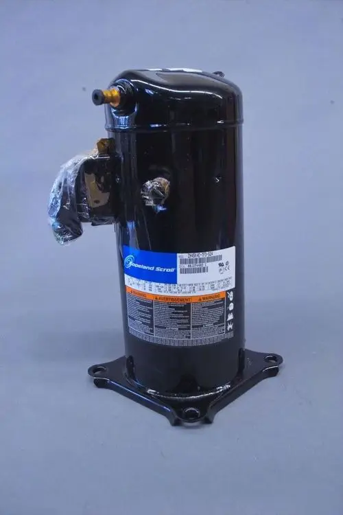 Schwarzer Scroll-Kompressor von Brötje mit mehreren Anschlüssen, montiert auf einer flachen Metallbasis. Sichtbare Label und Warnhinweise auf der Vorderseite.