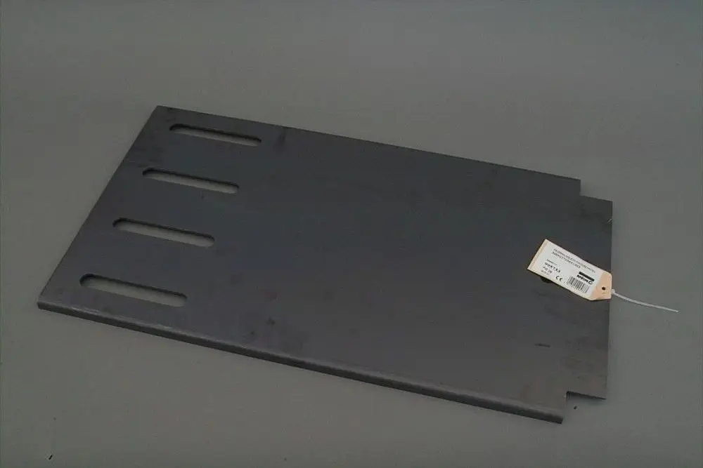 Schwarzes Metallblech mit vier Langlöchern und einem Etikett, geeignet für Anwendungen von Brötje, auf grauem Hintergrund.