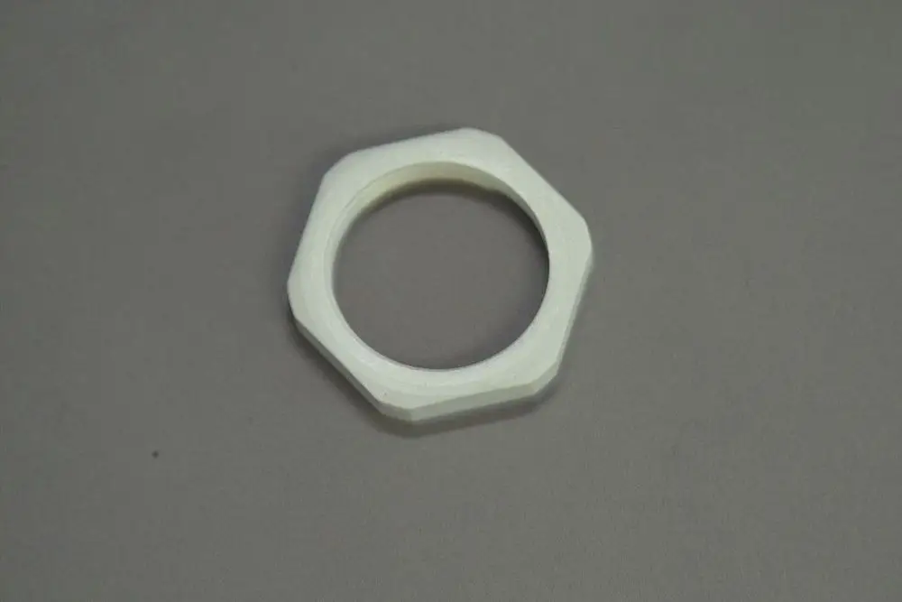 Bauteil von Brötje, augenscheinlich eine Mutter mit sechseckigem Design, gefertigt aus hellem Material, auf grauem Untergrund platziert.
