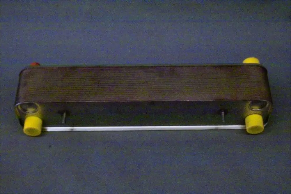 Brötje Wärmetauscher in rechteckiger Form, mit zwei farbigen Anschlüssen auf beiden Seiten, montiert auf einem grauen Untergrund.