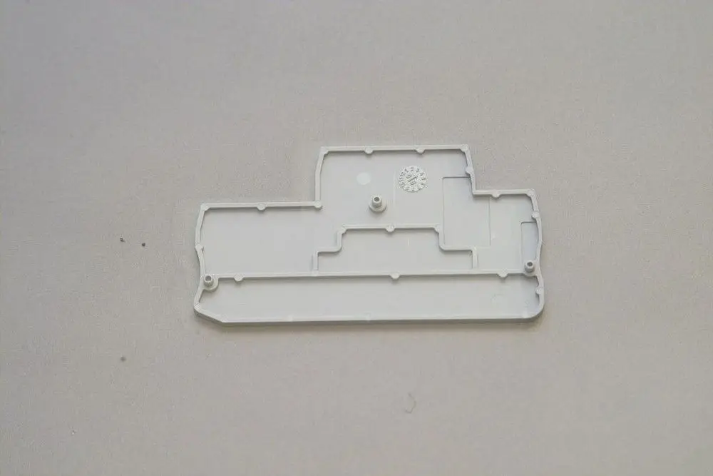 Weiße Kunststoffplatte von Brötje, mit Aussparungen und einer Vertiefung, möglicherweise als Endkappe für eine Verbindung oder Klemme gestaltet, vor hellem Hintergrund.