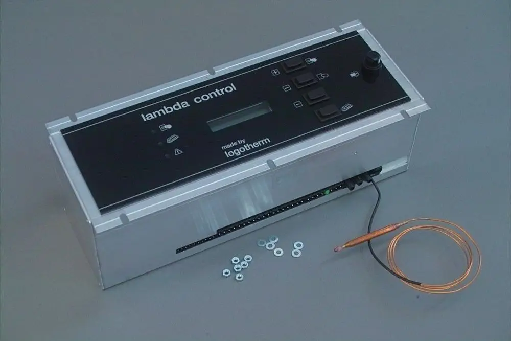 Lambda-Regelgerät von Brötje mit digitalem Display, mehreren Tasten und einem Sensorkabel, auf einer silbernen Basis liegend, umgeben von kleinen Unterlegscheiben.