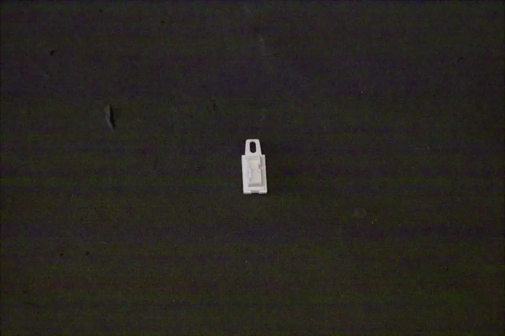 Weißer Kunststoffstecker mit Aussparungen, der möglicherweise für eine Brötje Bedieneinheit verwendet wird, auf dunkelgrauem Hintergrund.