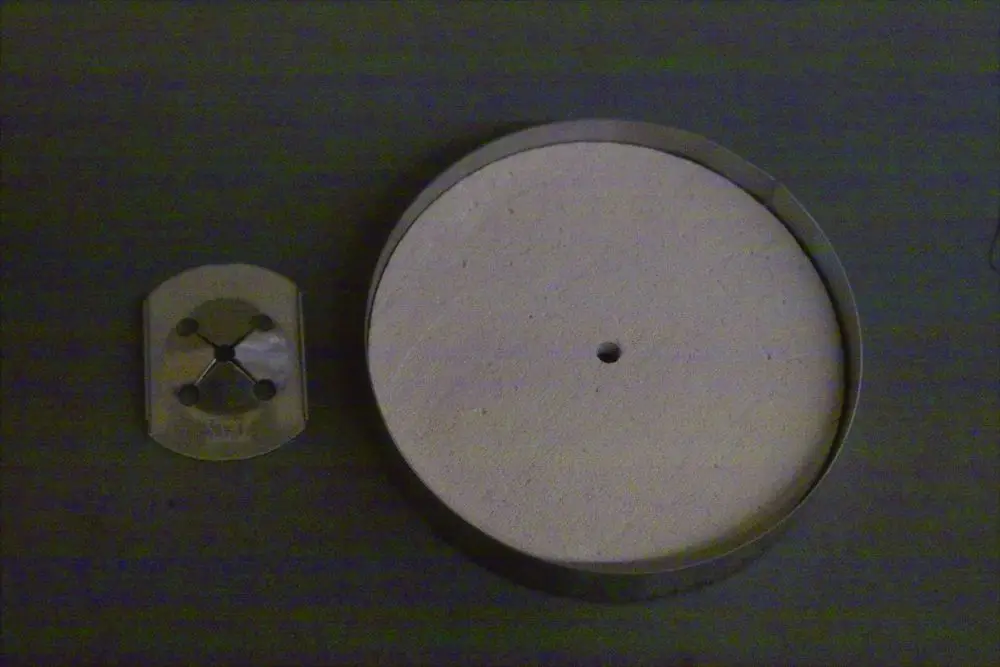 Brötje Abdeckkappe mit runder, flacher Oberfläche und mittigem Loch, daneben eine kleine Metallplatte mit vier Löchern zur Befestigung.