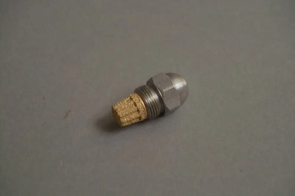 Brötje Düse mit metallischem Körper und goldenem Zubehörteil, liegt auf grauem Untergrund. Bestandteil einer Heizungsanlage oder ähnlicher Technik.