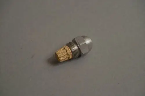 Brötje Düse mit metallischem Körper und goldenem Zubehörteil, liegt auf grauem Untergrund. Bestandteil einer Heizungsanlage oder ähnlicher Technik.