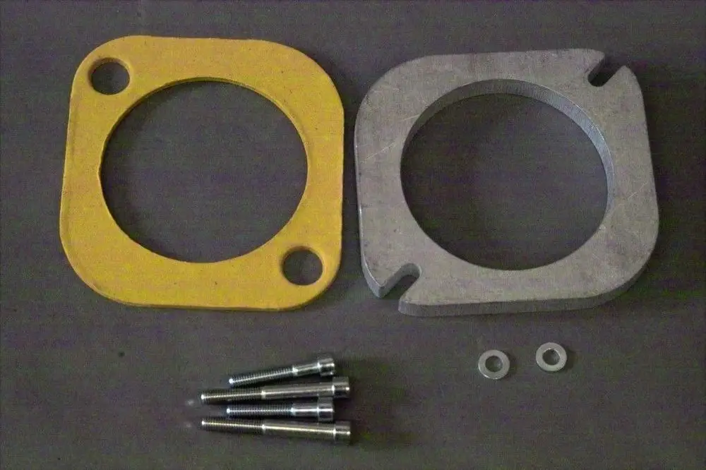 Brötje Kesselflansch aus gelbem Material und silbernem Metall, daneben mehrere Schrauben und Unterlegscheiben auf einem grauen Hintergrund.