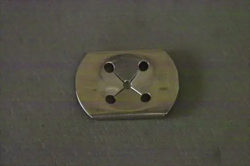 Brötje Halteklammer aus Metall mit vier Bohrungen und einer runden Aussparung in der Mitte, auf grauem Hintergrund abgebildet.