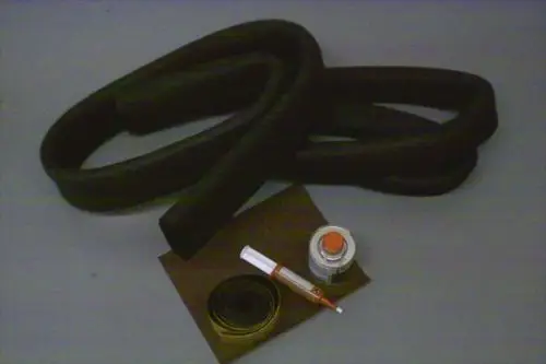 Schwarze, gewundene Schläuche, eine Dose mit rotem Deckel, ein kleiner Behälter mit farbiger Flüssigkeit und ein Stift auf braunem Untergrund. Brötje Reparatur-Set für Solekreise.