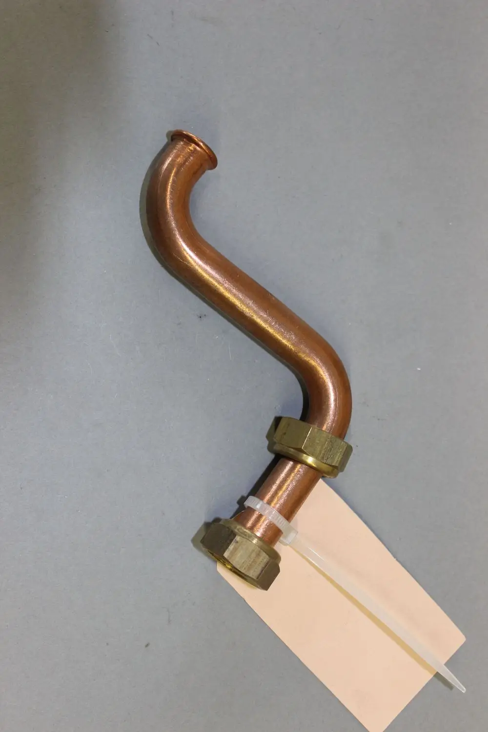 Brötje Warmwasserrohr mit einer gebogenen Form und zwei Metallverschraubungen. Am Rohr befindet sich ein Etikett.