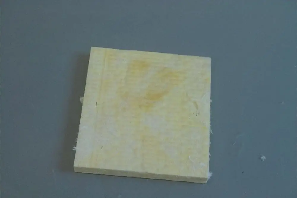 Brötje Dichtung in quadratischer Form aus gelbem Material, erkennbar an der strukturierten Oberfläche, liegt auf grauem Untergrund.