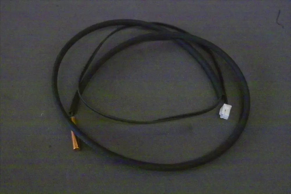 Brötje Verdichterrückflussfühler, mit einem schwarzen Kabel und einem senkrechten Metallanschluss, auf dunklem Untergrund.