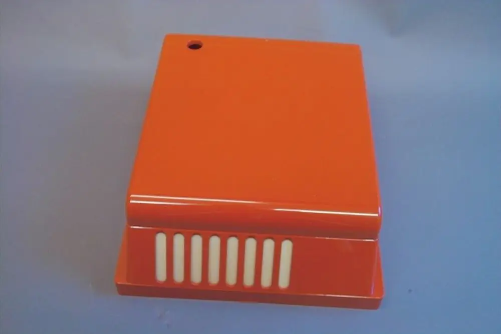 Brötje Brennerhaube in Orange, quadratische Form mit seitlichen Lüftungsschlitzen und kleiner Öffnung oben. Oberfläche glänzend.
