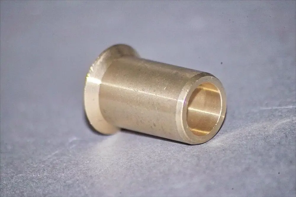 Brötje Düse aus Messing, zylindrische Form mit einem dicken Flansch am Ende und hohlem Inneren. Auf leicht strukturiertem Hintergrund.