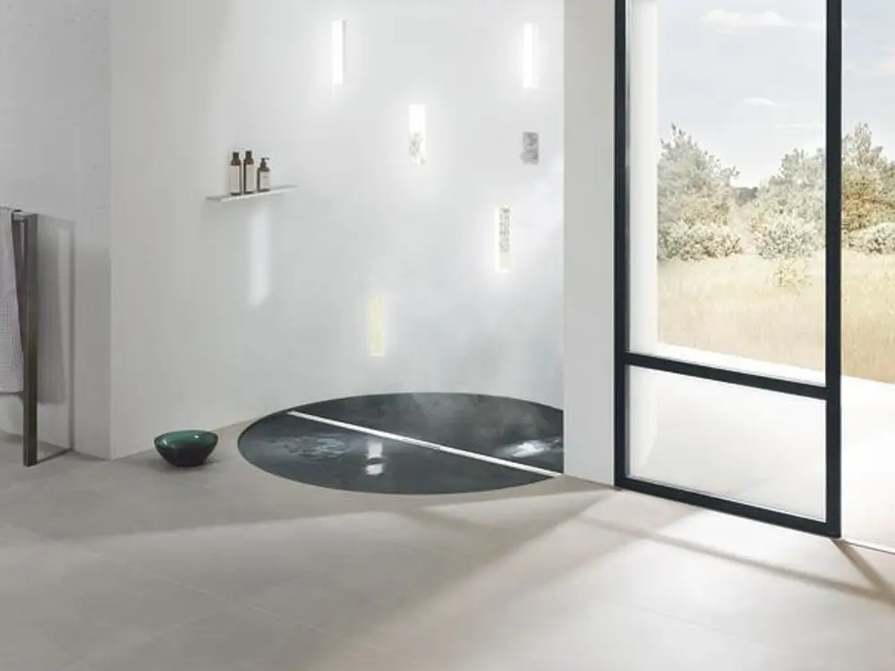 Bodenablauf von Dallmer in einem modernen Badezimmer, eingebaut in eine runde Dusche mit minimalistischem Design, umgeben von hellen Fliesen und natürlichem Licht.