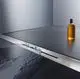 Dallmer Duschrinne in mattem Edelstahl, integriert in eine ebene Fläche. Wasser fließt durch die Rinne, während eine Flasche im Hintergrund sichtbar ist.