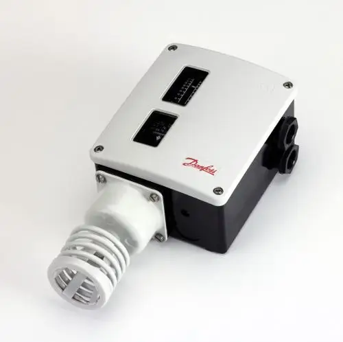 Raumthermostat von Danfoss mit zwei Anzeigeinstrumenten und einer angeschlossenen Fühlerspirale, montiert auf einer weißen Unterlage.