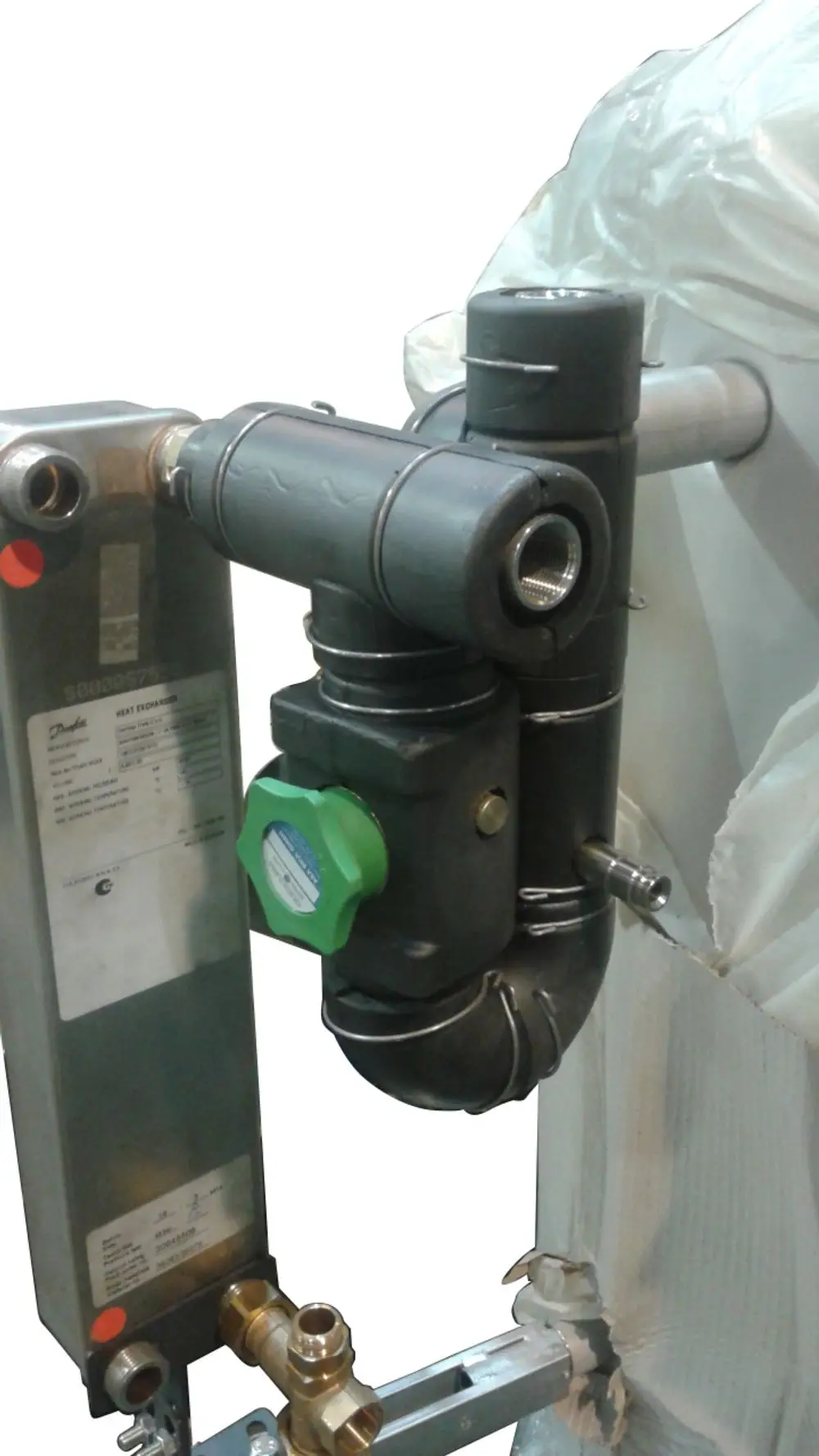 Wärmeübertrager von Danfoss mit metallischer Oberfläche. Eingänge und Ausgänge für Rohrverbindungen, ausgestattet mit einer grünen Regelungsvorrichtung.