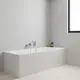 GROHE Wandmontage-Armatur mit zwei Griffen, installiert über einer Wanne, vor grauer Wand und hellem Holzboden, ergänzt durch eine Duschbrause und Accessoires auf dem Wannenrand.