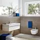Badezimmer mit weißen Wandfliesen, einem hängenden Waschbecken von Grohe sowie einem Bidet. Blaue Handtücher und eine Vase mit Ästen sind dekorativ platziert.